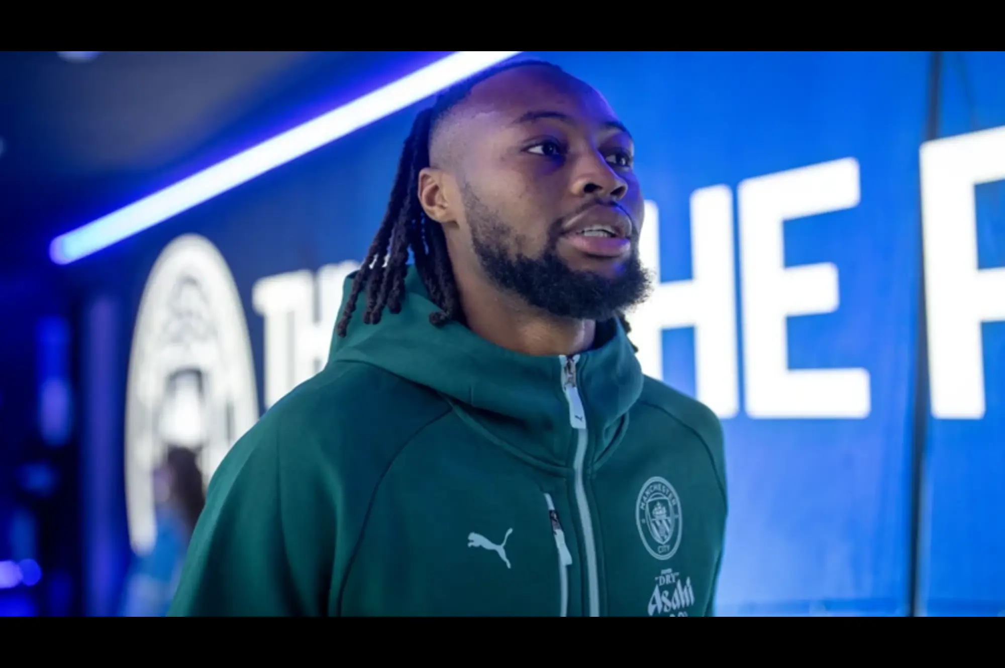A professional football player wearing a green training jacket inside a stadium tunnel before a competitive match