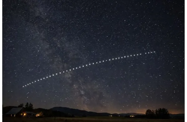 Starlink satellites appearing in a straight line across the night sky above a rural area.