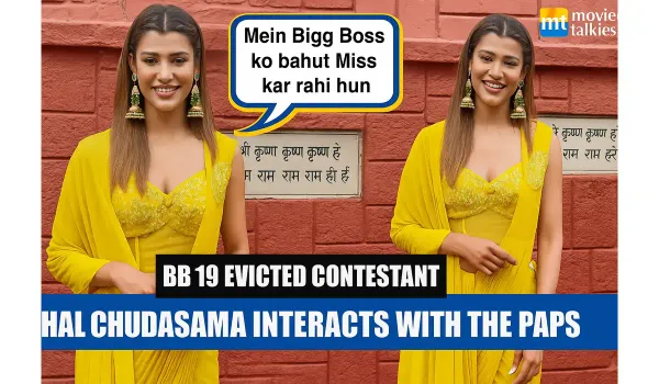 The image shows a young woman wearing a bright yellow traditional fusion outfit standing outside near a red brick wall. She i